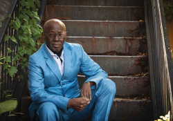 A photograph of Boubacar Boris Diop sitting on stairs looking at the camera