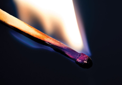 A close-up photograph of a wood match burning