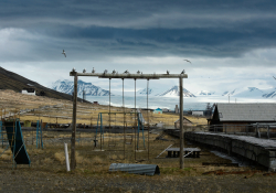 A desolate playground sits in the foreground on dried grass with a glacier in the background