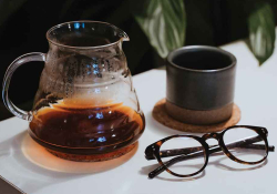 A photograph of a clear tea pot, a tea mug, and a pair of glasses on a table
