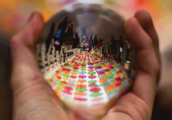 A polished steel ball held in a hand reflects a long table with colored plates on it