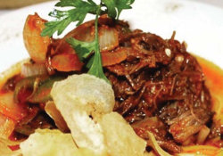 A portion of stewed meat, garnished with parsley, served with a small bed of chips
