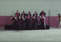 A still image from the video to Childish Gambino's "This is America," featuring a choir of African-Americans singing on riser as Gambino emerges into the frame from the right