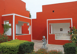 Two buildings, painted brightly red, intersect like angular puzzle pieces with a small green courtyard between them