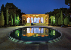 A photograph of an ornate building, lit up at night, which is also reflected in a pool in the courtyard