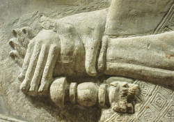 A bas-relief sculpture of hands clasping across the wrist