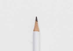 The tip of a white pencil laying on a piece of white paper