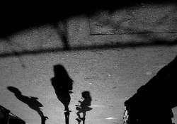 A black and white photograph of human shadows on the pavement