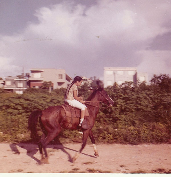 A faded color photograph of a young Margarita riding a horse in Cuba