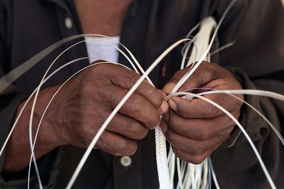 A close up on a pair of hands weaving a straw hat