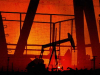 A dramatic photo of numerous oil wells pumping in a dark orange sunset