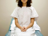 A woman in a hospital gown sitting on an examination table with her hands folded in her lap