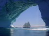 A photograph of a sail boat on the water as seen from inside of an icy cave