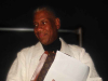 A photograph of André Leon Talley, clad in a white linen jacket. His gaze looks off the left side of the panel