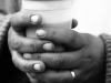 A black and white photograph of a pair of hands grasping a plastic coffee cup