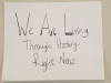 A hand-written sign. Text reads: We are living through history right now.