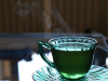 A photograph of a cup of tea. The cup is clear and the tea is green