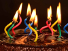 A photo of a chocolate birthday cake, its candles lit but strangely warped