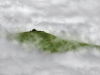 A photograph looking up at a house on a grass covered hill, swathed in fog