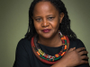 A photograph of Edwidge Danticat, wearing black offset by a colorful scarf, against an olive background