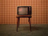 A photograph of an old tube style television on a wooden stand in front of a old-fashioned brown plaid wallpaper