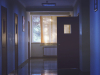 A hallway in a hospital with an door open just before a window lit by the sun