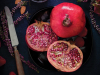 Looking down on a table that has two pomegranates on it, one cut, one uncut, with the knife that opened the one up laying beside it.