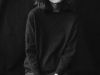 A black and white photo of a woman in a dark sweatshirt and black jean looking at the camera