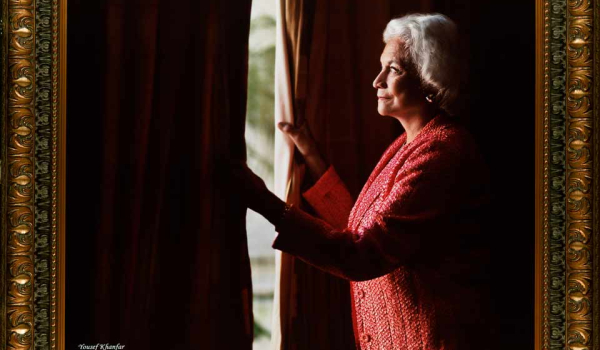 A photograph of Justice Sandra Day O'Connor peering out through a heavy curtain to the daylight outside