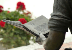 Sculpture of person reading a book in a park with red flowers