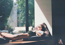 A photograph of a person lying in the sun looking out a window