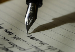 A pen hovers above lined paper with words (text unimportant) preceding