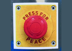 A red button mounted on a yellow kackground. Text around the button reads: Press for Peace