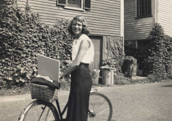A black and white photo of Sylvia Plath with her bicycle smiling at the camera