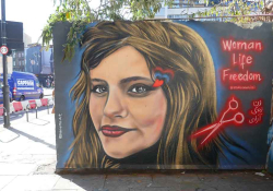 A mural of a woman's face with a pair of scissors near her head rendered in dark red. Text reads: Woman. Life. Freedom.