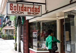 A photograph of a woman in a green jacket entering a book store. A sign above reads, “Solidaridad”