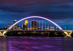 The skyline of Minnepolis seen through an arched bridge suspended over purple water