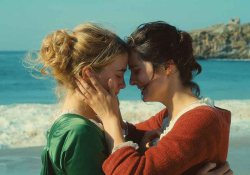 A still photograph from Portrait of a Lady on Fire that features two women standing on a beach, holding one another and pressing foreheads