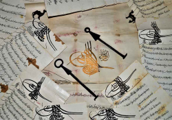 Pieces of paper, covered in Arabic writing, are scattered on a table. A pair of keys sits near the center