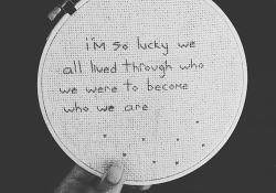 Words needlepointed into cloth on a hoop. The words read I'm so lucky we all lived through who we were to become who we are
