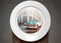 A plate, mounted to a slate gray wall, with the image of a vintage car in the center. The wall beneath the plate is discolored.
