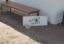 A photograph of a hand-lettered sign propped up against a low wooden bench. Text reads: Marfa Books
