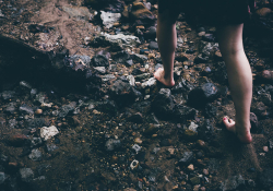 A woman walking over rocks with bare feet.